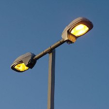 A twin head parking lot light on its pole against a clear blue sky