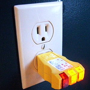 A receptacle tester plugged into a wall outlet showing its indicator lights during an electrical inspection