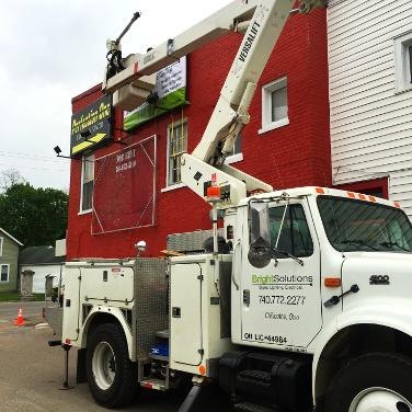 The Bright Solutions bucket truck with its boom raised, servicing a sign on a red brick storefront in Chillicothe